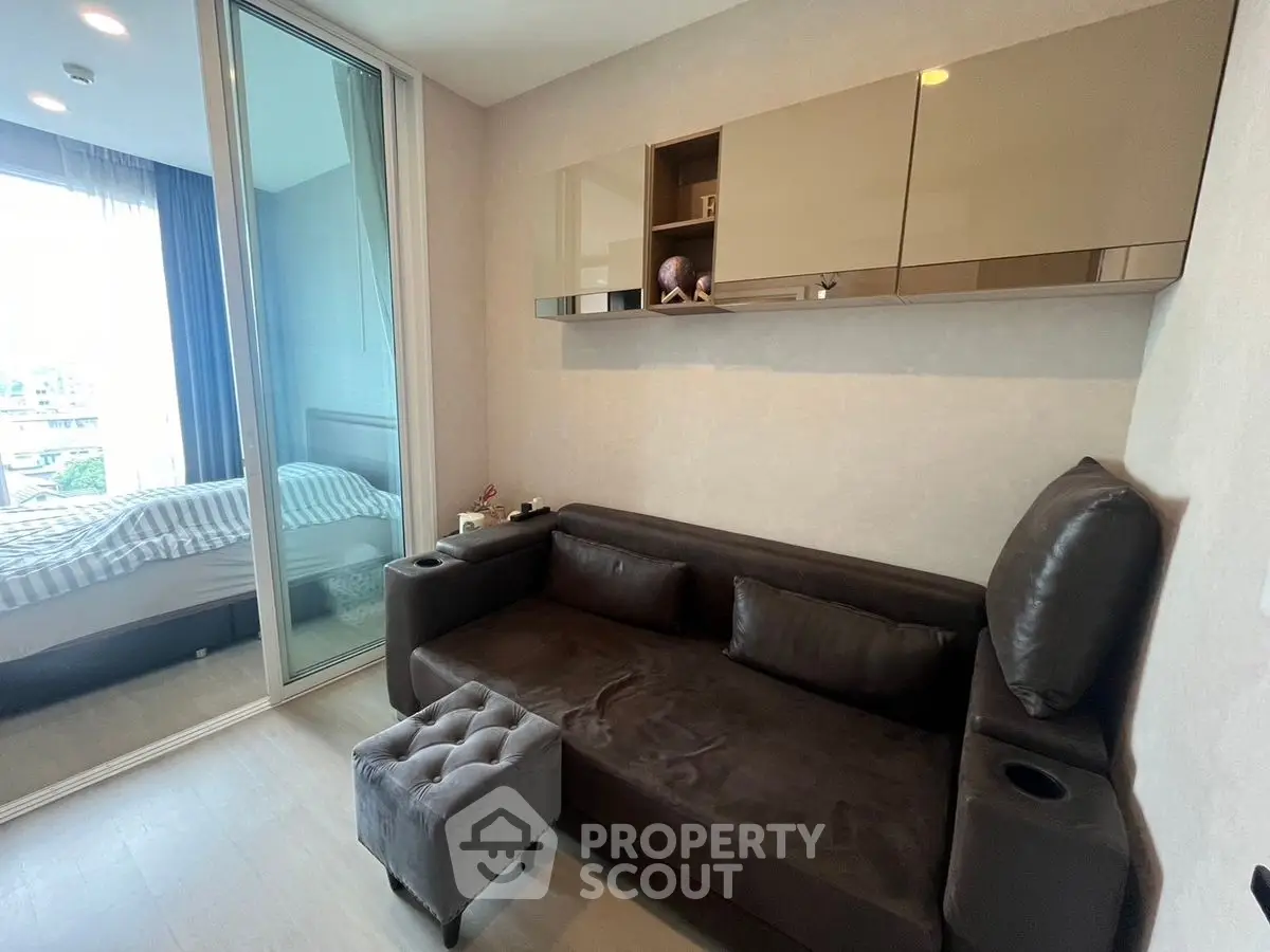 Modern living room with sleek sofa and glass partition leading to a cozy bedroom.