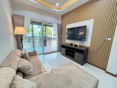 Modern living room with cozy sofa and large TV, featuring stylish decor and natural light from balcony.