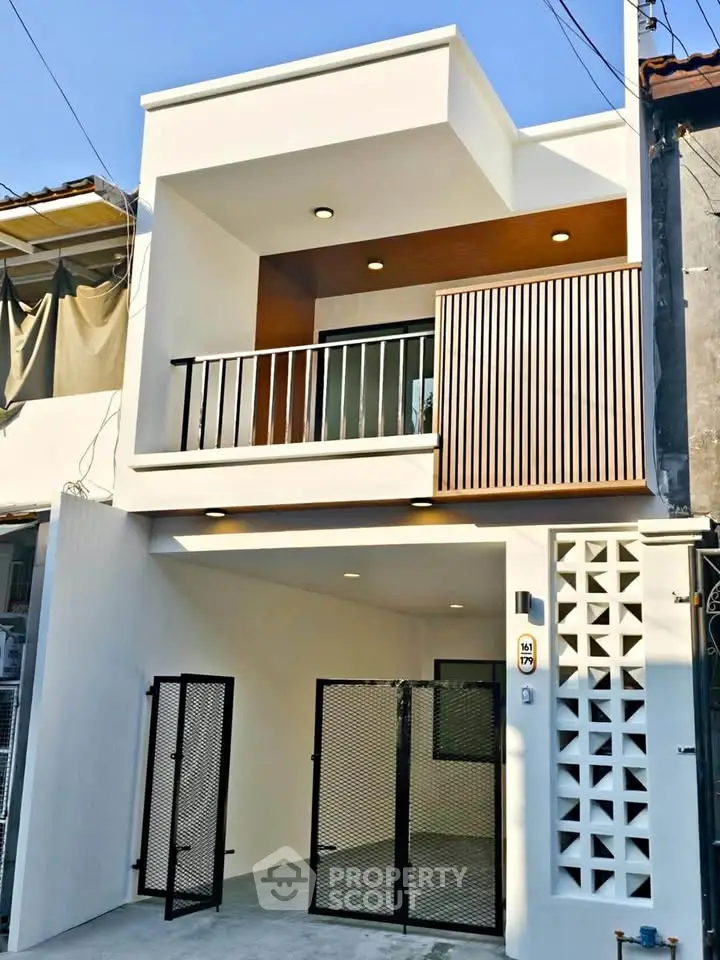 Modern two-story house with stylish balcony and gated entrance.