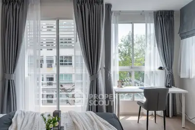 Bright bedroom with large windows and study area, featuring elegant gray curtains and modern decor.
