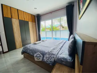 Spacious bedroom with modern decor and pool view, featuring large windows and stylish wardrobe.