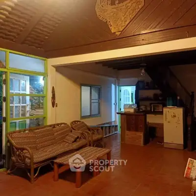 Charming rustic living space with terracotta tiles and wooden ceiling beams, featuring wicker furniture and a cozy kitchenette.