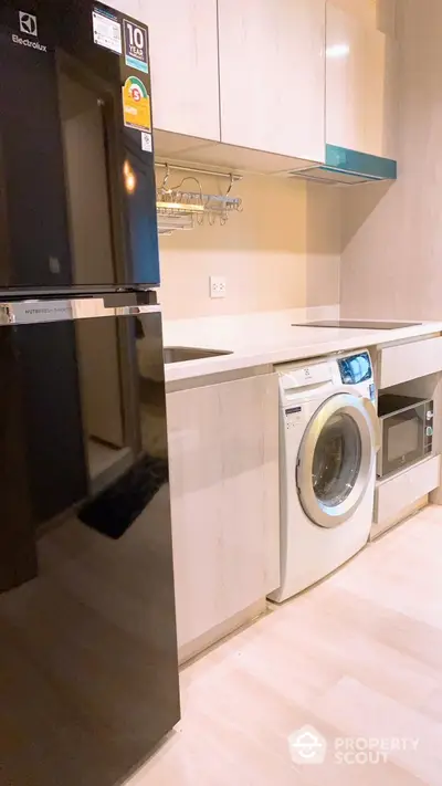 Modern kitchen with appliances including fridge, washing machine, and microwave in sleek cabinetry.