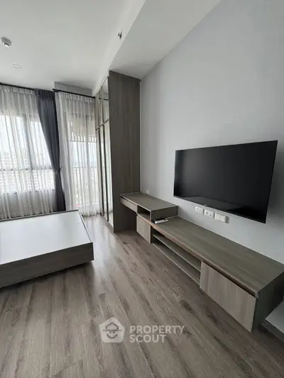 Modern bedroom with sleek wooden flooring and wall-mounted TV, featuring large windows for natural light.