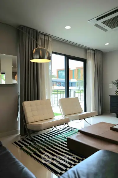 Modern living room with stylish furniture and large windows offering natural light and outdoor view.