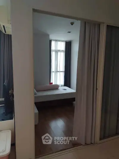 Cozy bedroom with large window and wooden flooring in modern apartment.