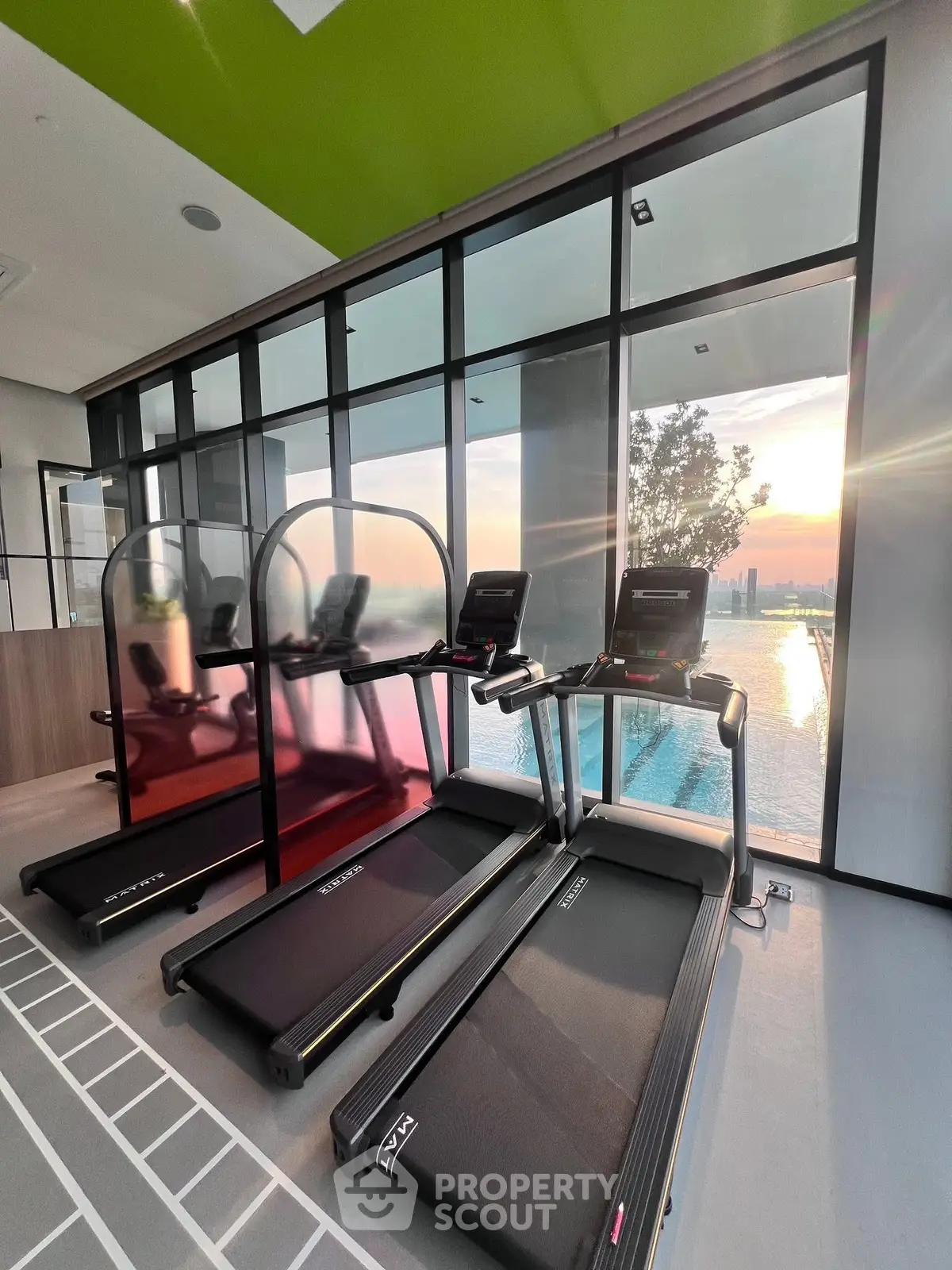 Modern gym with treadmills and stunning city view through large windows at sunset.
