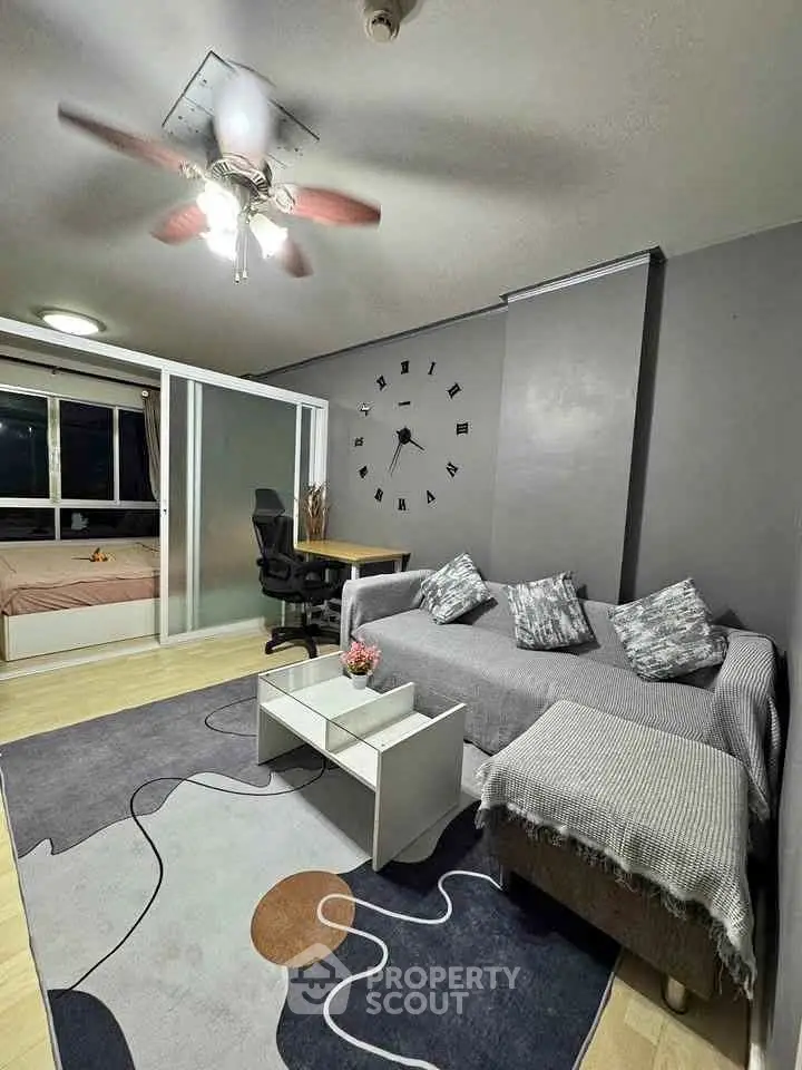 Modern living room with stylish decor and cozy seating area, featuring a unique wall clock and ceiling fan.