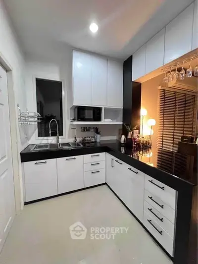 Modern kitchen with sleek white cabinets and black countertops, featuring a stylish open layout and contemporary lighting.