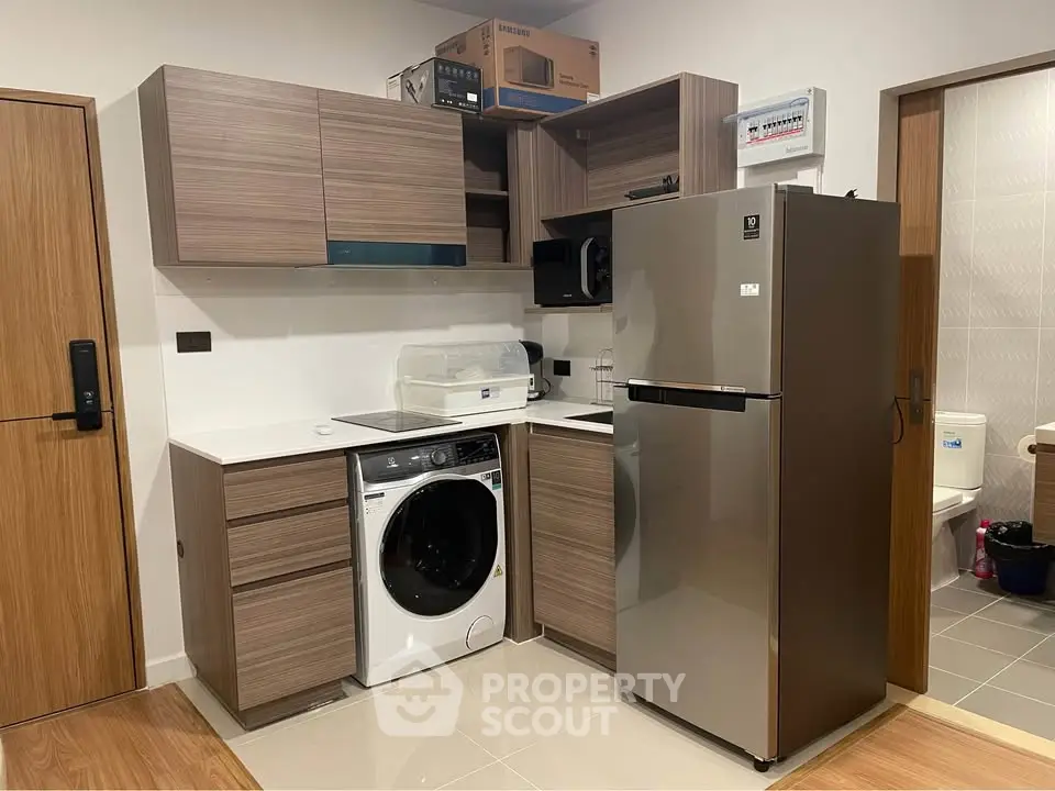 Modern kitchen with sleek wooden cabinets, integrated washing machine, and stainless steel fridge.