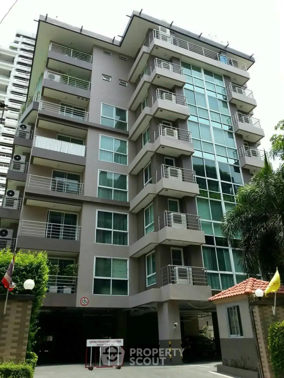 Modern multi-story apartment building with balconies and lush greenery in urban setting.