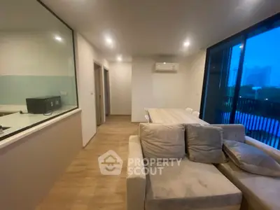 Modern living room with cozy sofa and dining area, featuring large windows and wooden flooring.