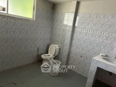 Spacious bathroom with tiled walls and floor, featuring a toilet and sink area.