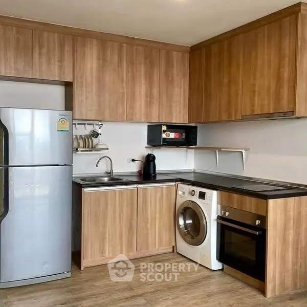 Modern kitchen with wooden cabinets, washing machine, fridge, and oven in cozy apartment.