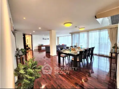 Spacious open-plan living and dining area with elegant wooden flooring and large windows.
