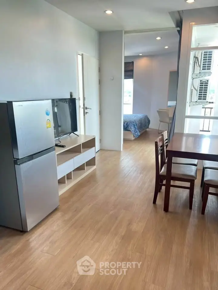Modern apartment interior with open layout, featuring dining area, TV, and view into bedroom.