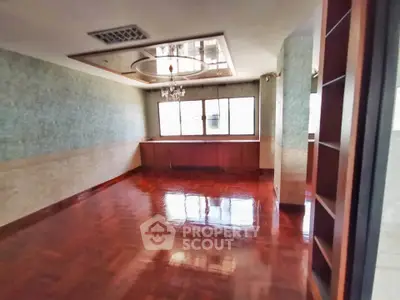 Spacious empty room with polished wooden floors and large windows in a modern apartment.
