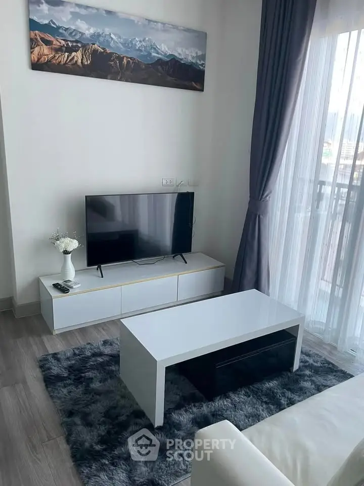 Modern living room with sleek furniture and mountain artwork, featuring a cozy rug and large window with curtains.