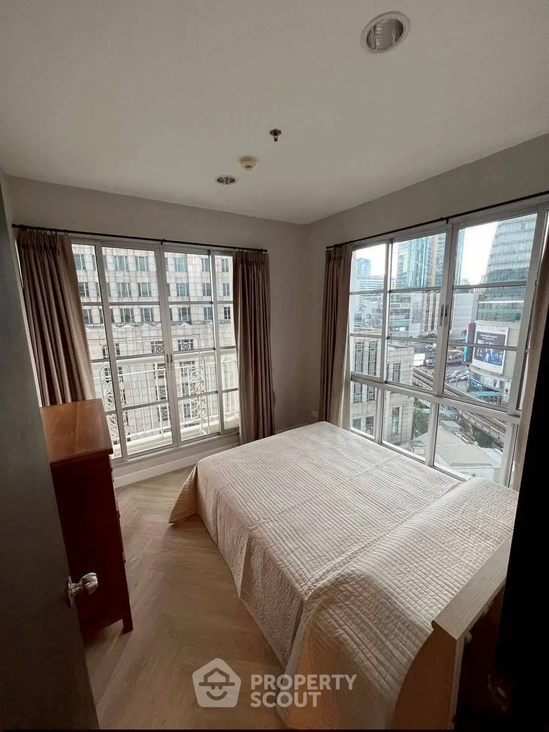 Bright corner bedroom with large windows offering city views in modern apartment.