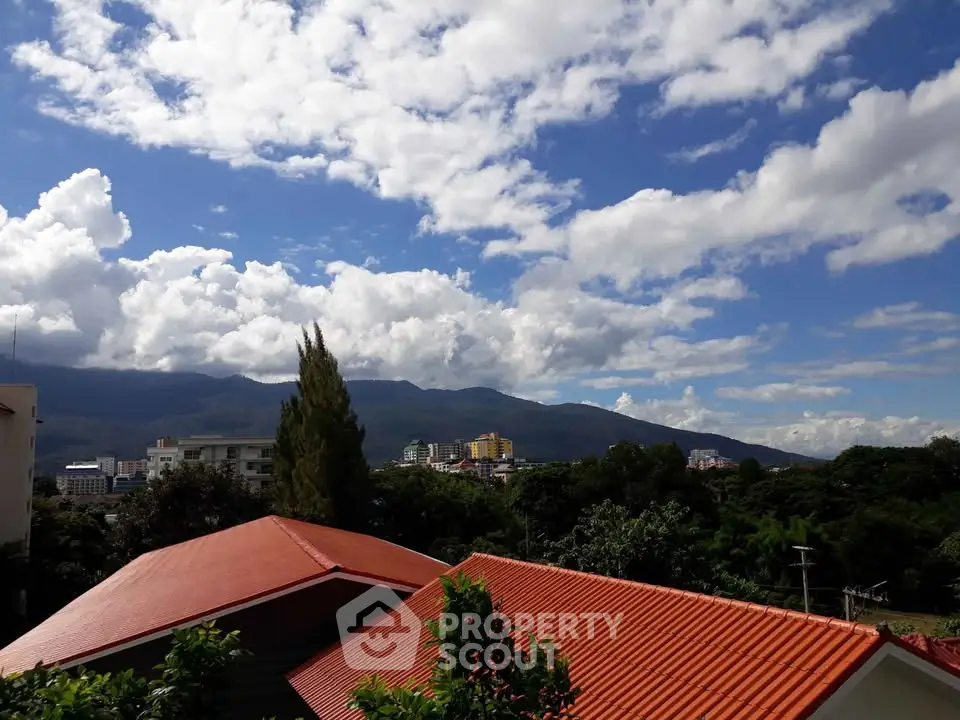 Scenic view of rooftops and lush greenery with mountains in the background under a vibrant blue sky.