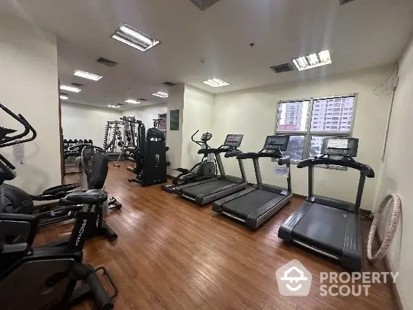 Spacious gym with modern equipment and city view in luxury apartment complex.