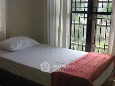 Cozy bedroom with natural light and garden view, featuring a single bed and elegant curtains.