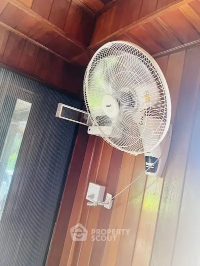 Wall-mounted fan in a wooden-paneled room corner, showcasing ventilation feature.