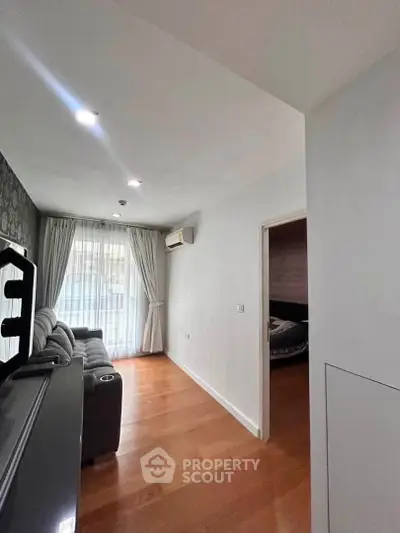 Spacious living room with wooden flooring and natural light, featuring a cozy sofa and air conditioning.