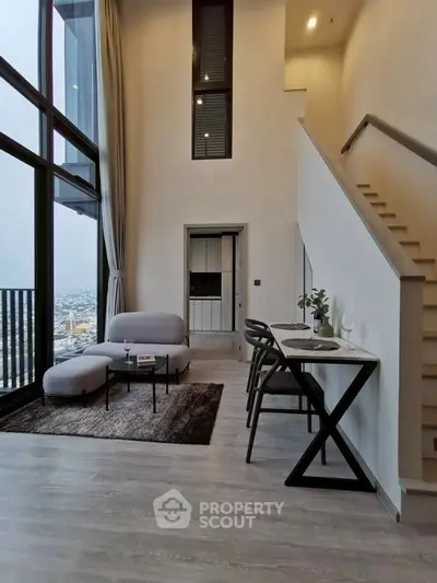 Modern loft apartment with high ceilings and city view, featuring stylish furniture and elegant staircase.