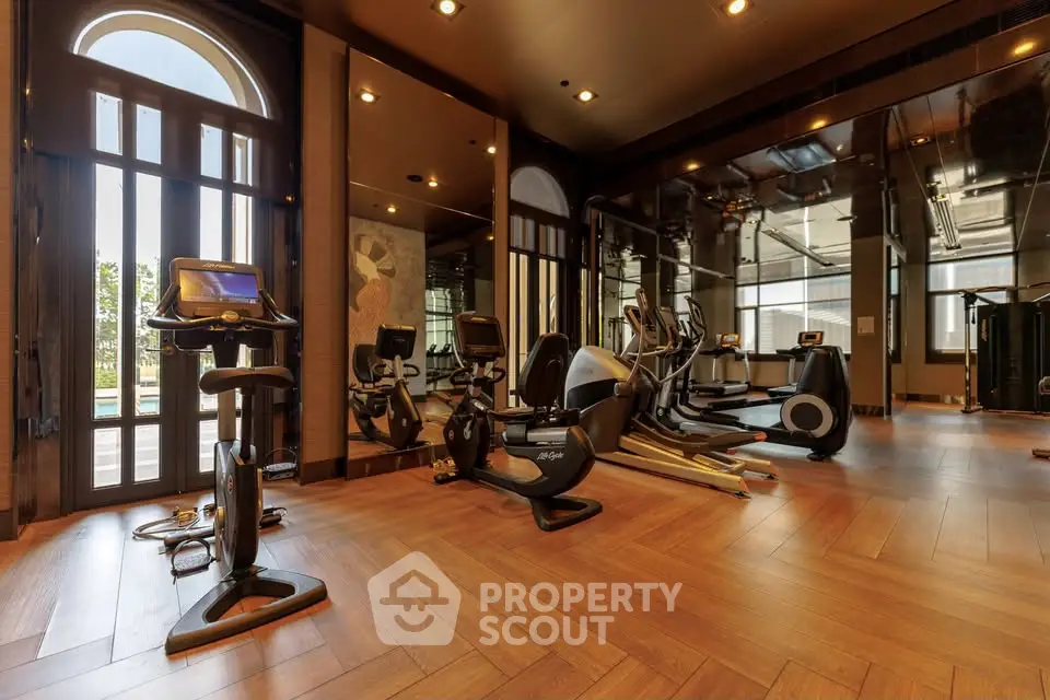 Luxurious gym with modern equipment and wooden flooring in upscale residential building.