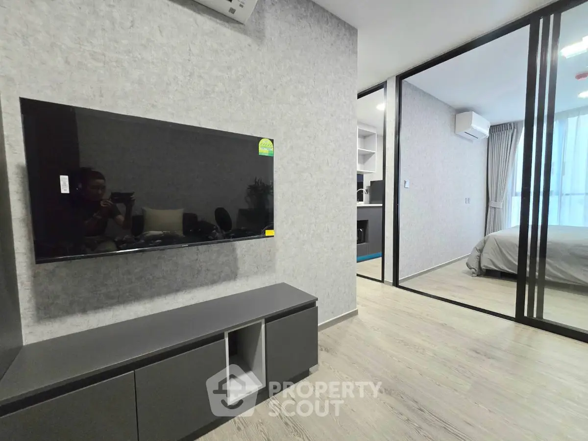 Modern living room with wall-mounted TV and view into stylish bedroom