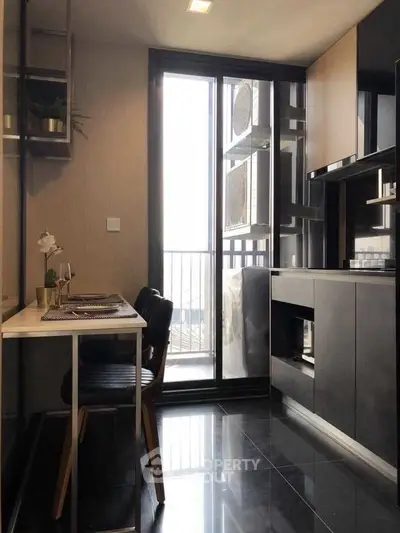Modern kitchen with sleek black cabinetry and dining area, featuring a balcony view.