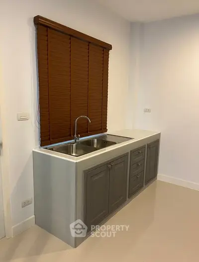 Compact kitchen space with modern gray cabinetry and stainless steel sink, complemented by warm brown window blinds in a well-lit room.