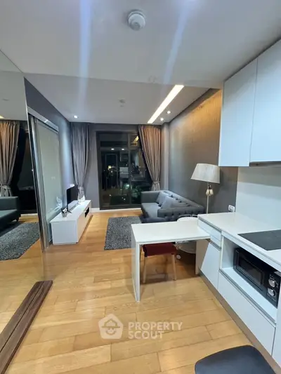 Modern living room with sleek kitchen and cozy seating area, featuring elegant lighting and hardwood floors.