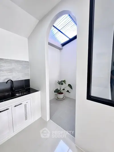Modern kitchen with sleek black countertop and stylish archway leading to a bright patio with skylight.