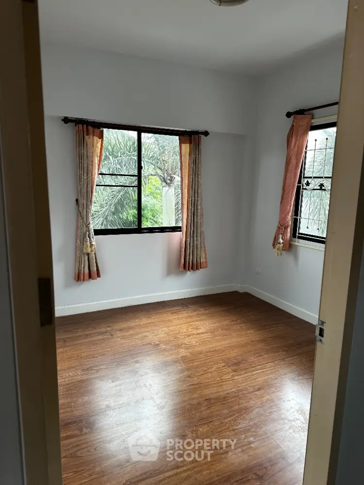 Bright empty room with wooden flooring and large windows, perfect for customization.