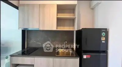 Modern compact kitchen with sleek cabinetry and stainless steel sink, featuring a refrigerator and electric cooktop.