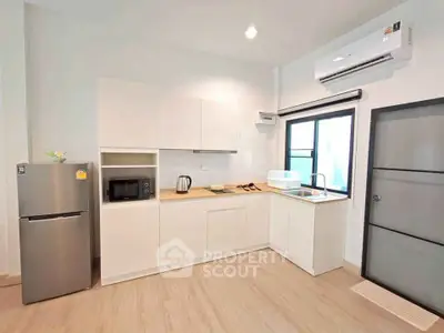 Modern kitchen with sleek appliances and minimalist design, featuring a fridge, microwave, and air conditioning.