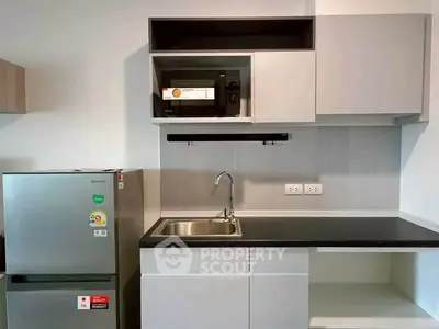 Modern kitchen with sleek cabinetry, stainless steel fridge, and built-in microwave.