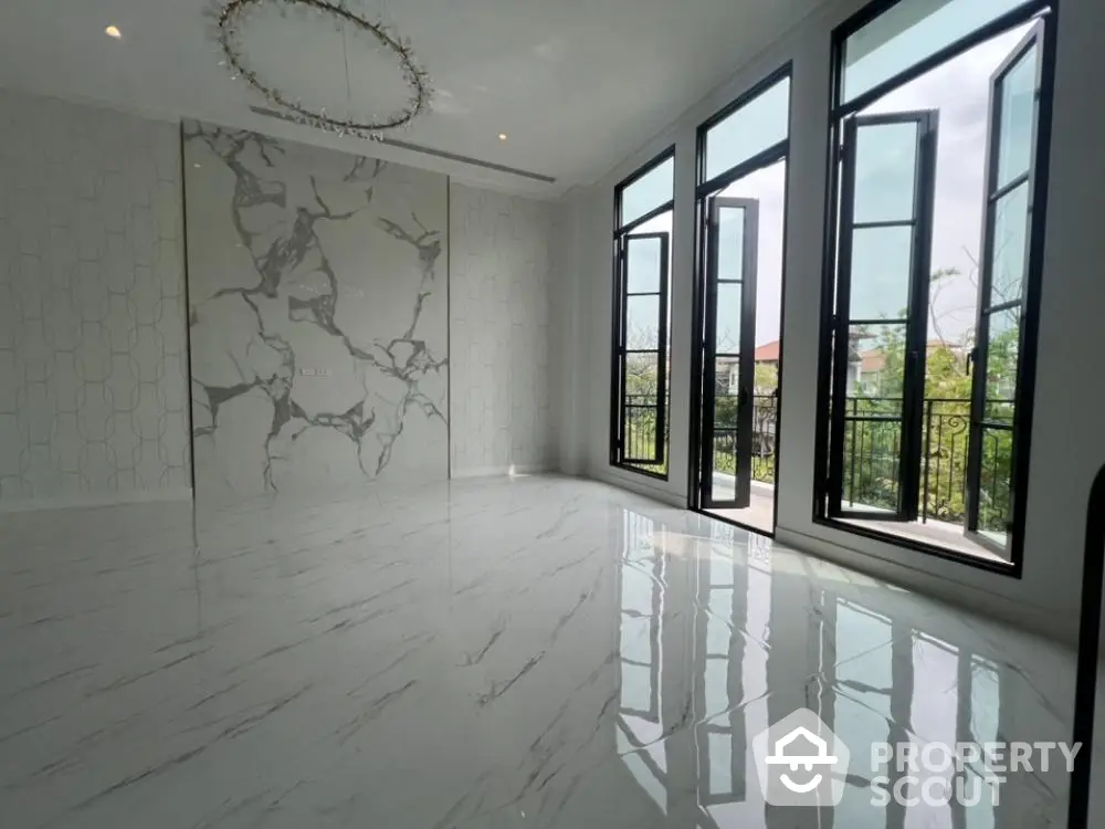 Spacious and bright living room with high-gloss marble flooring, elegant marble wall design, and large black-framed windows offering ample natural light.