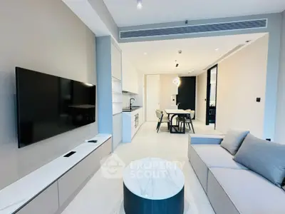 Modern living room with sleek furniture and open kitchen layout, featuring a large flat-screen TV and stylish decor.