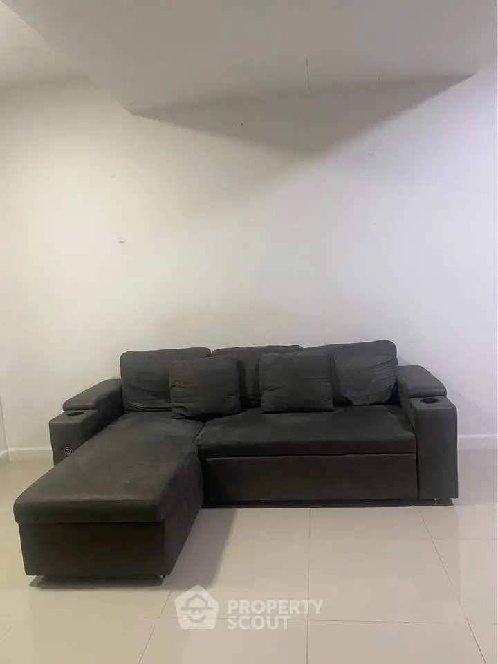 Spacious living room with modern dark gray sectional sofa and sleek tile flooring.