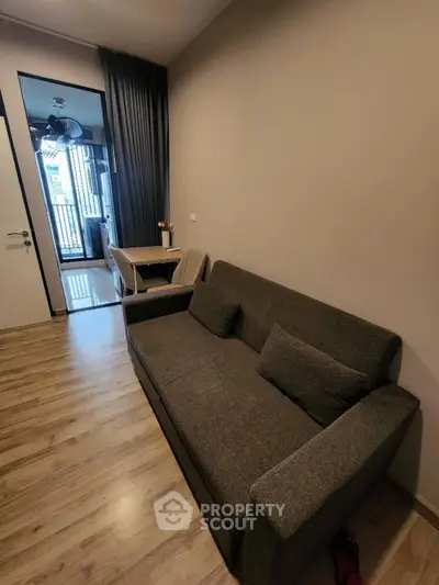 Modern living room with cozy sofa and wooden flooring, leading to a bright balcony area.