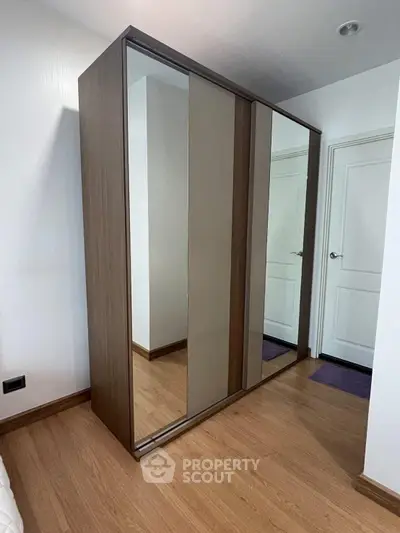 Spacious bedroom with modern mirrored wardrobe and elegant wooden flooring.