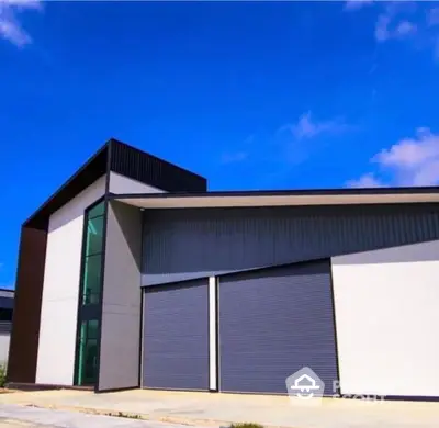 Modern industrial building with sleek design and large roller doors under a clear blue sky.