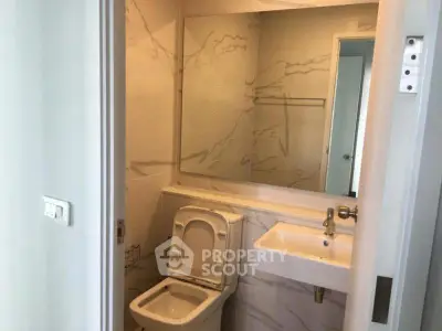 Modern bathroom with sleek design and elegant marble walls, featuring a compact toilet and stylish sink.