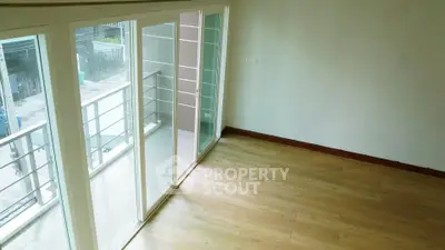Spacious room with large sliding glass doors leading to a balcony, featuring light wood flooring.