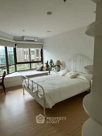 Spacious bedroom with large window and cozy seating area, perfect for relaxation.
