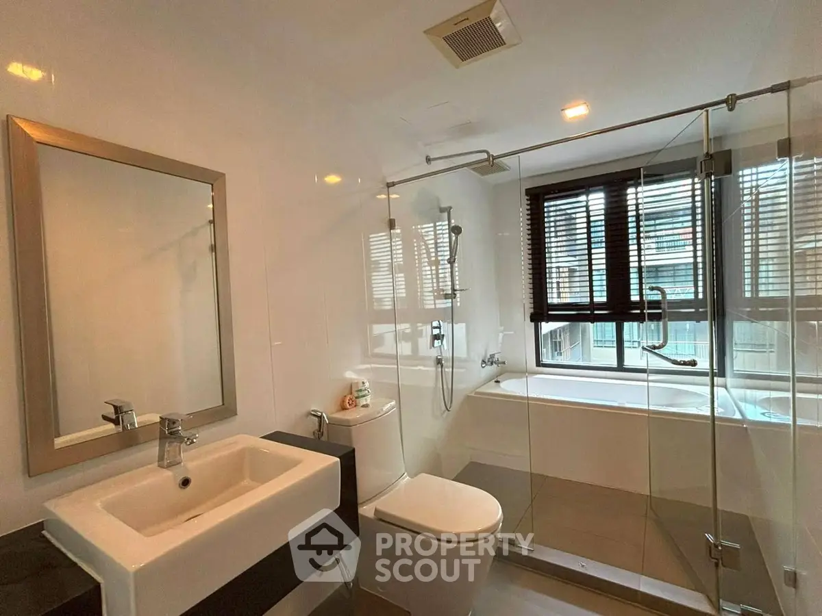 Modern bathroom with glass shower and bathtub, featuring sleek fixtures and natural light.