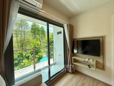 Modern living room with balcony view and wall-mounted TV, featuring large glass doors and lush greenery outside.
